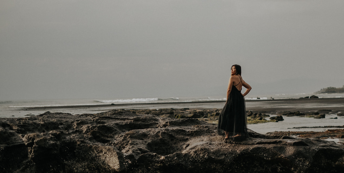 digital nomad sarah on the rocky beaches of Bali in a floor length black dress