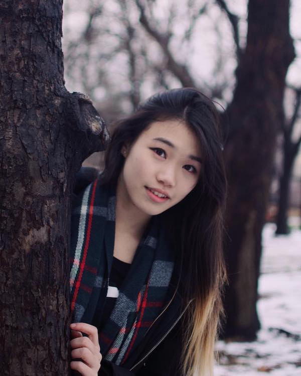 Asian woman peaking from behind a tree in the winter