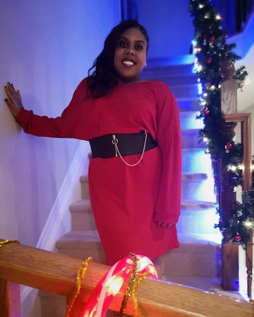 Black woman dressed up in red dress on set of stairs decorated for Christmas